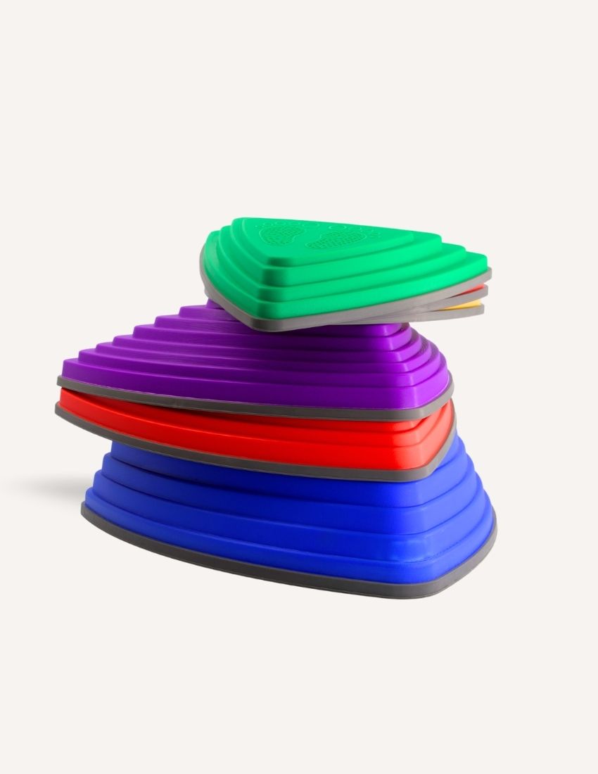 A stack of colorful Stepping Stones from Sensory Play Australia is displayed, perfect for children to develop their gross motor skills. The top stone features a green design with an embossed foot, followed by purple, red, blue, and yellow stones in descending order. These stones are ideal for children's play or physical activities.