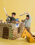 A cardboard castle craft kit emerging from a green and brown box. The castle is partially assembled with grey cardstock and includes additional pieces such as a horse, a carriage, and a cardboard sword. Perfect for imaginary play and cognitive development, the Imaginary Play: Noble Knight Kit by The Play Way includes an instruction booklet.