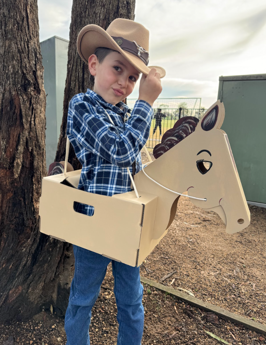 A cardboard castle craft kit emerging from a green and brown box. The castle is partially assembled with grey cardstock and includes additional pieces such as a horse, a carriage, and a cardboard sword. Perfect for imaginary play and cognitive development, the Imaginary Play: Noble Knight Kit by The Play Way includes an instruction booklet.