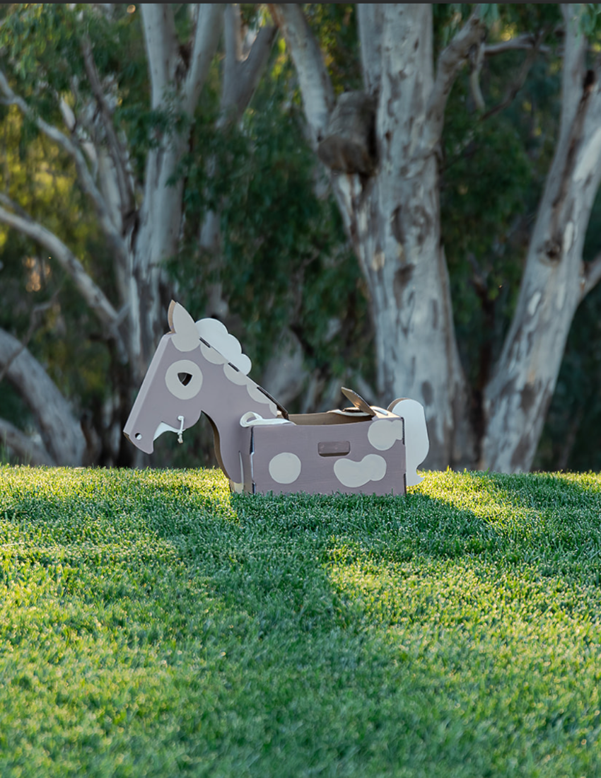 A cardboard castle craft kit emerging from a green and brown box. The castle is partially assembled with grey cardstock and includes additional pieces such as a horse, a carriage, and a cardboard sword. Perfect for imaginary play and cognitive development, the Imaginary Play: Noble Knight Kit by The Play Way includes an instruction booklet.