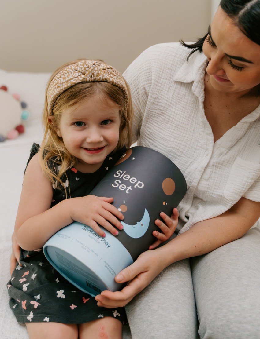 A round, light blue box labeled "Sensory Play Australia" contains the "Sleep Set," which includes a white cylindrical bottle labeled "Melo Dream," a brown spray bottle labeled "Melo," and a folded light blue fabric item, possibly an eye mask or pillowcase.