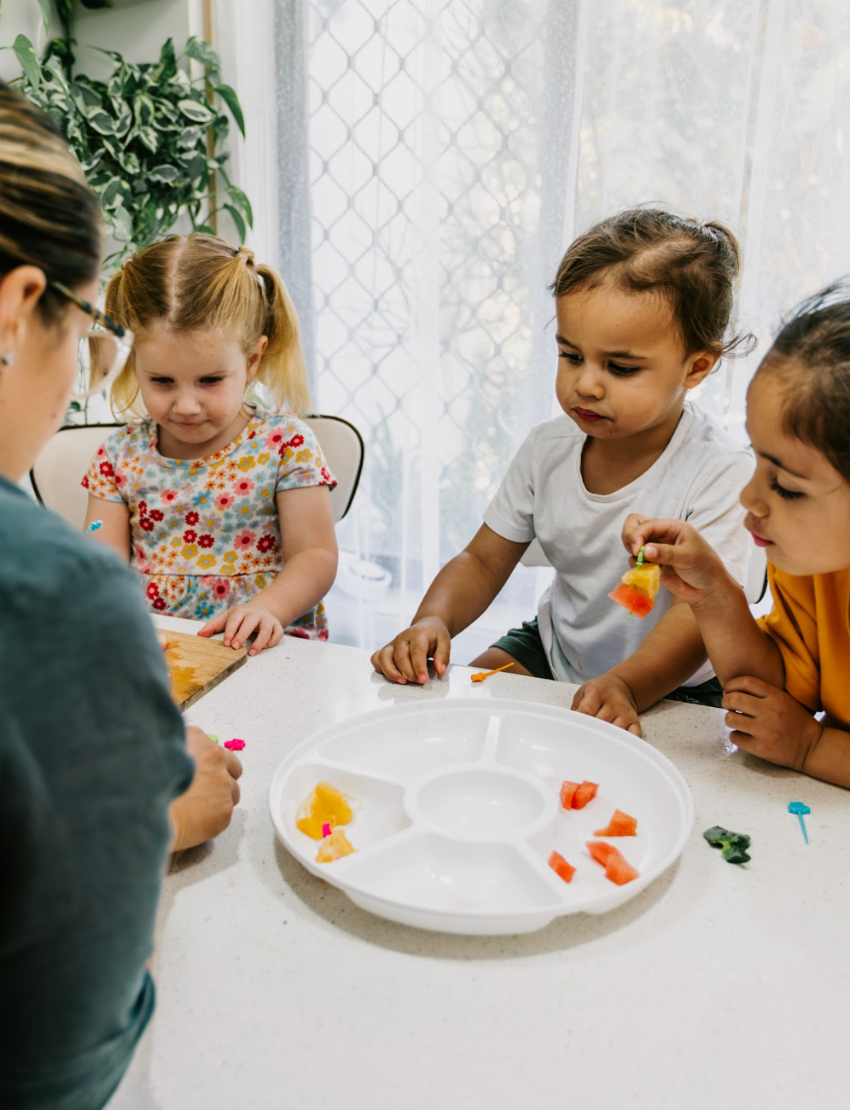 The image displays a set of educational and toy items from The Play Way's Food Exploration Kit, which includes colorful cards, a compartment tray, markers, a pop-it toy, rolling pins, a cutting tool, and a box. This kit appears to be crafted for sensory enjoyment and creative learning activities during mealtimes.