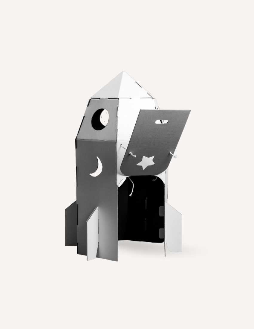 Cardboard rocket playhouse with moon and star cutouts and an open door.