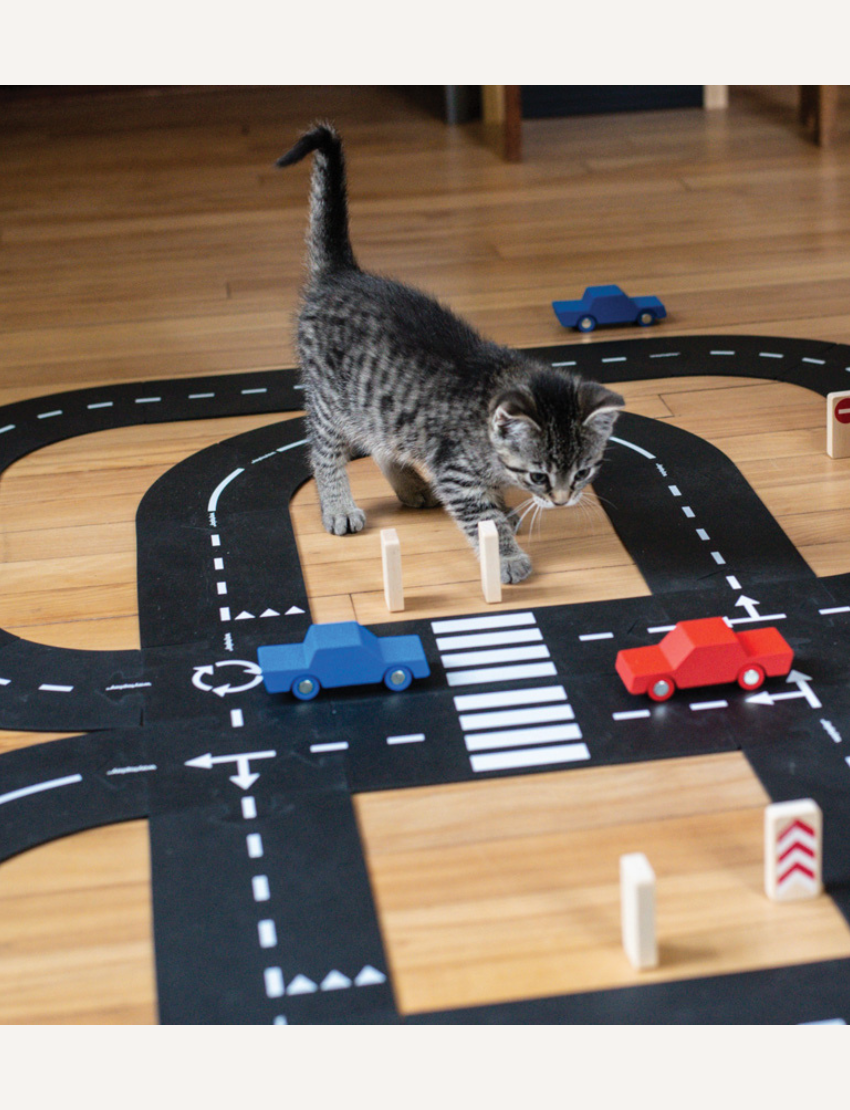 The image displays the "King Of The Road Car Edition" toy set by Waytoplay, which includes flexible road pieces and two wooden cars in red and blue. In the background, there is a box depicting a child playing with and assembling the road.