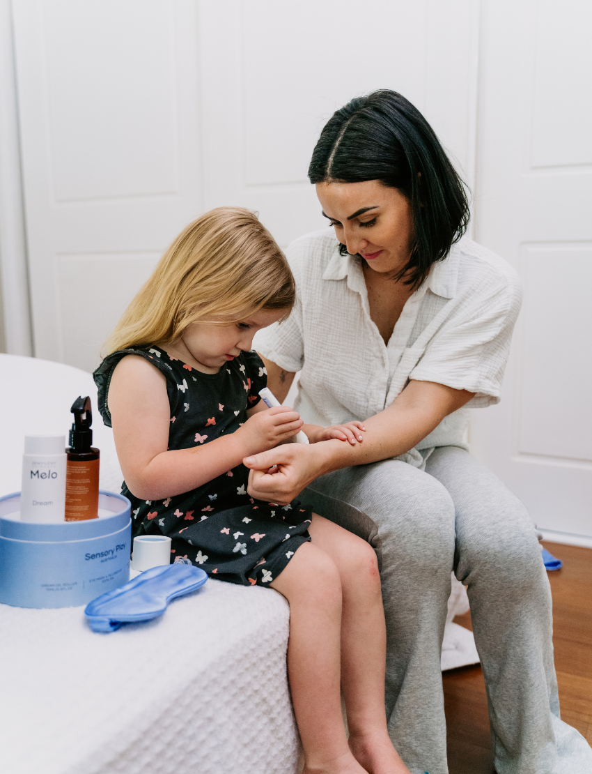 A round, light blue box labeled "Sensory Play Australia" contains the "Sleep Set," which includes a white cylindrical bottle labeled "Melo Dream," a brown spray bottle labeled "Melo," and a folded light blue fabric item, possibly an eye mask or pillowcase.