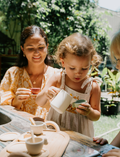 A child indulges in imaginative play with Sensory Play Australia's wooden Teatime Set, featuring a tray, three cups, a teapot, and spoons. Nearby is a metal sink with a draining area on the countertop to enhance cognitive skills through interactive fun.