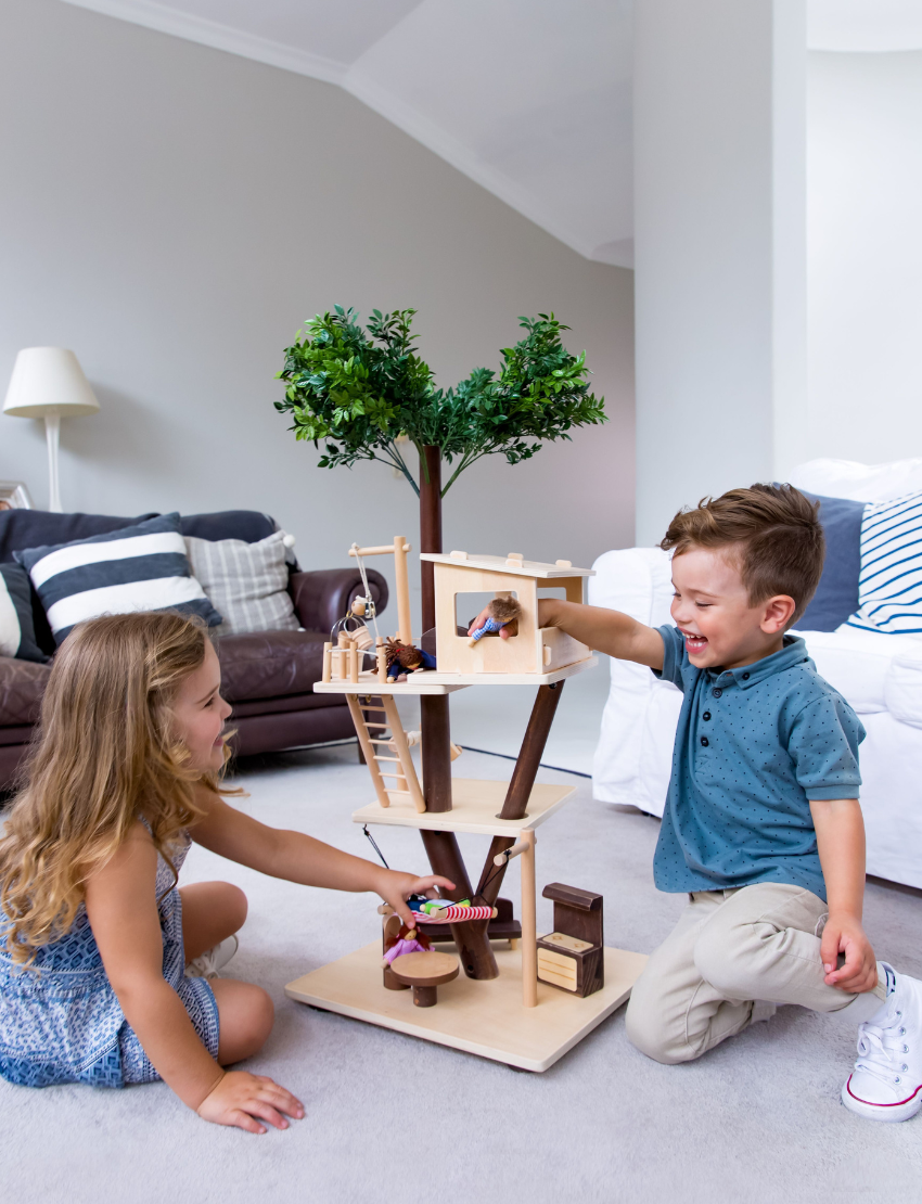 The Ever Earth Tree House is a wooden toy with three levels, featuring miniature furniture, figures, and accessories. It includes a swing on one side and a rope ladder on the opposite side. At the top, there is a small artificial tree surrounded by figures posed in various activities.