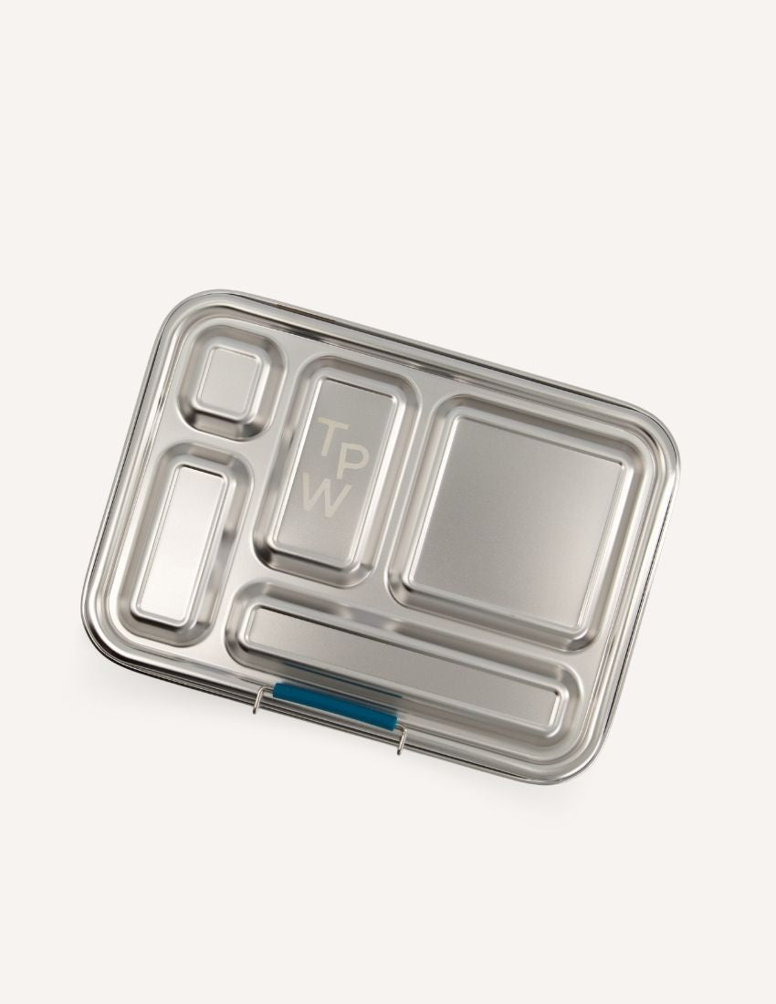 Introducing the Lunch Buddy Bento Set by The Play Way, a sleek rectangular stainless steel lunchbox with multiple compartments. The top right section is larger than the others, with "TPW" engraved in the central compartment. It features a silicone seal lid, rounded edge design, clasp closure, and a polished metallic finish.