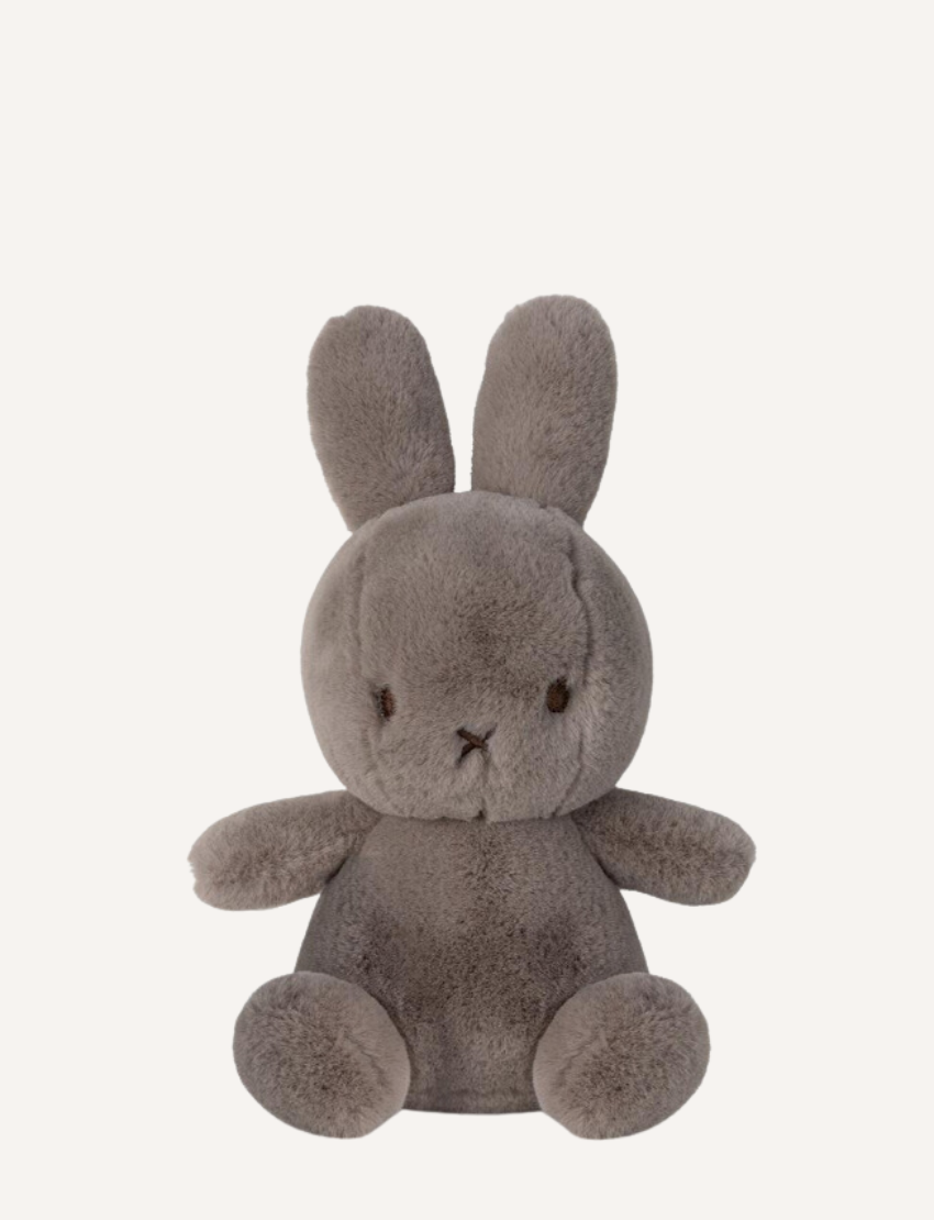 Two Miffy "Cozy Miffy" plush bunnies are showcased against a plain background. The left one is light cream, while the right is dark gray; both are made from recycled polyester and feature simple facial details with small black eyes and a cross-shaped nose and mouth.