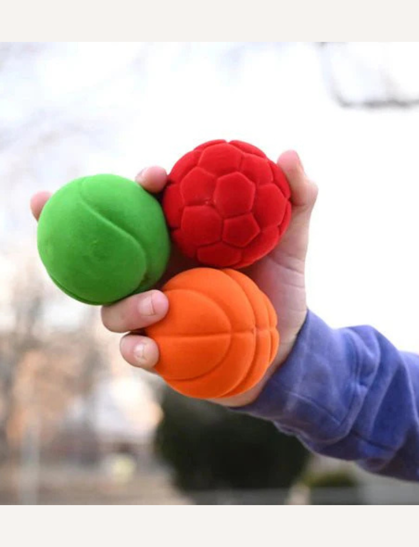 Image showcasing the Small Sports Balls Set of 3 by Rubbabu. The set includes three colorful foam balls in orange, red, and green, each featuring a unique texture. The packaging is a white box adorned with vibrant designs and branding.