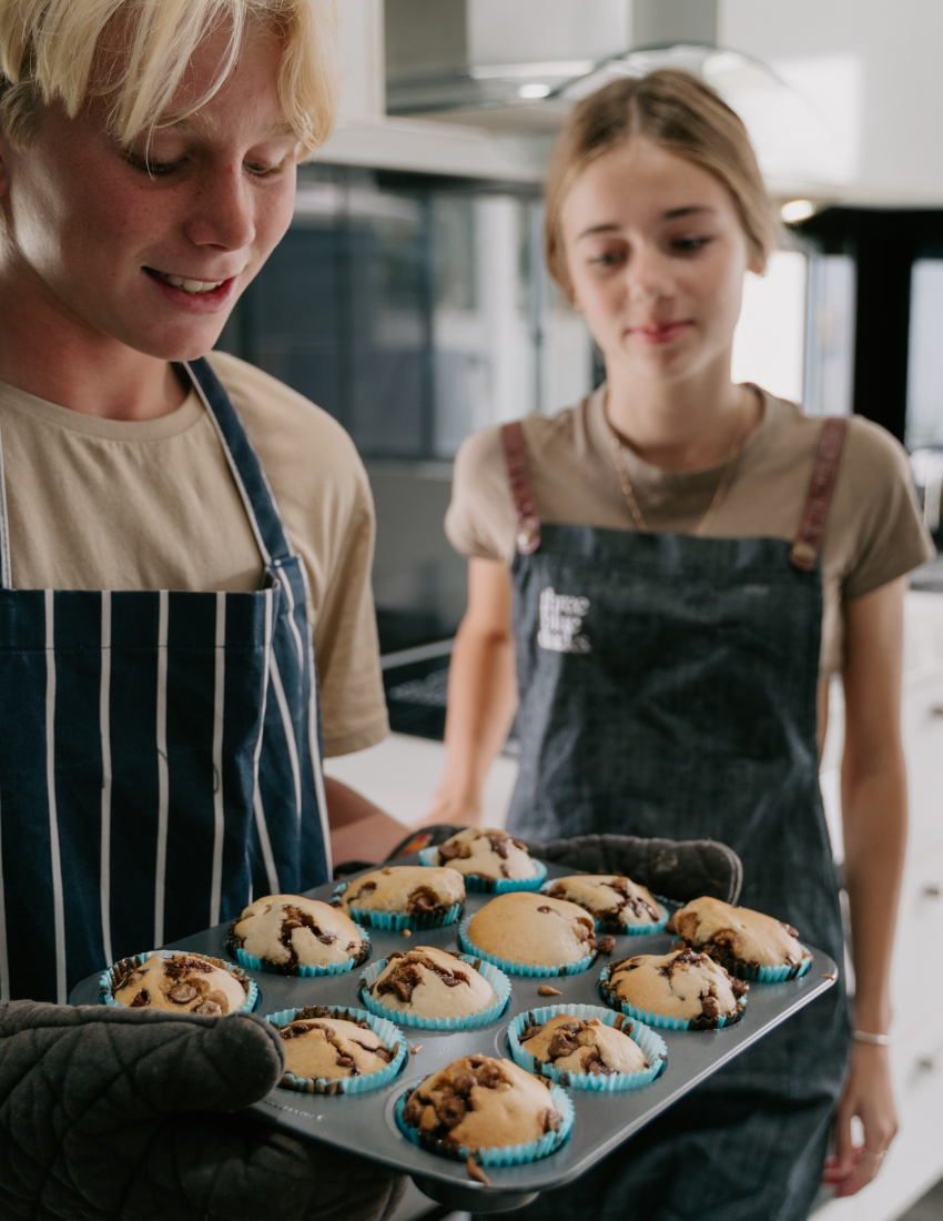 The "Getting Started with Baking Kit" by The Play Way is open. Inside this children's baking kit, you'll find a black apron and a black towel, both featuring "The Play Way" branding, colorful measuring cups, a recipe sheet for culinary adventures, and a black muffin tray.