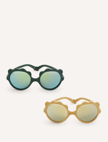 Two pairs of Ki ET LA's LION sunglasses for 2-4-year-olds are displayed. One, made in France, has dark frames with blue-tinted lenses; the other features light yellow frames with gold-tinted lenses. Both have round, unbreakable lenses and decorative frame accents.