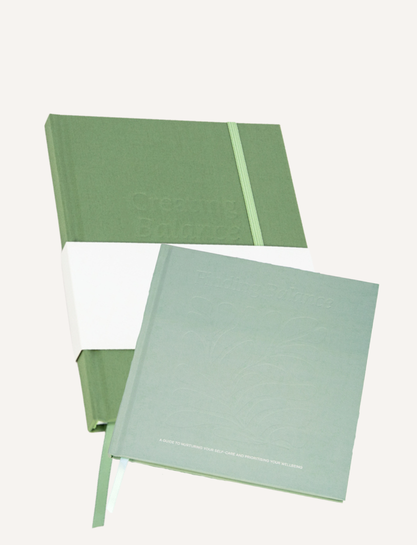 Three open Belucci journals with green covers are displayed. The nearest book, the Balance Journal & Guidebook, features a leaf illustration and the word "Gratitude." Its pages contain text and lined sections for writing. All books rest against a plain background.