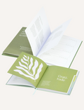 Three open Belucci journals with green covers are displayed. The nearest book, the Balance Journal & Guidebook, features a leaf illustration and the word 