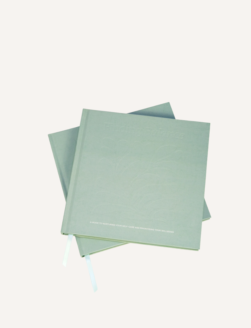 Two Belucci "Finding Balance Guidebook" hardcovers in light gray, stacked on a plain white backdrop, showcase embossed titles and attached light blue ribbon bookmarks.