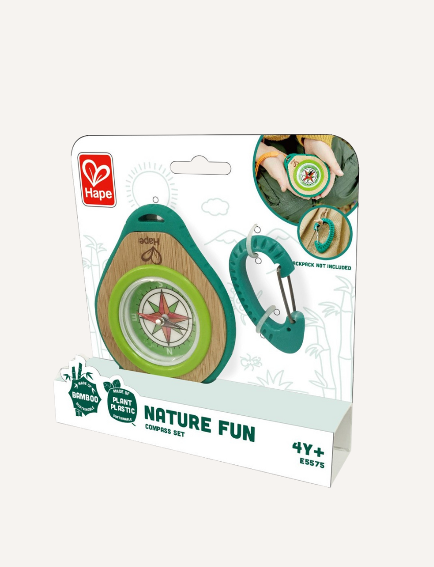 The Hape Compass Set includes a round compass featuring a red arrow, elegantly housed in a wooden base. It is encased in green and teal rubber with an attached orange wrist strap, and comes with a teal carabiner clip placed beside it.