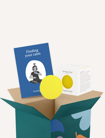 A teal box from The Play Way containing the Calm Story Kit is open, revealing a yellow squishy ball and a small booklet titled "Finding your calm." Both items are positioned visibly above the box. The box itself features a simple design with abstract shapes, ideal for sensory soothing and emotional regulation.