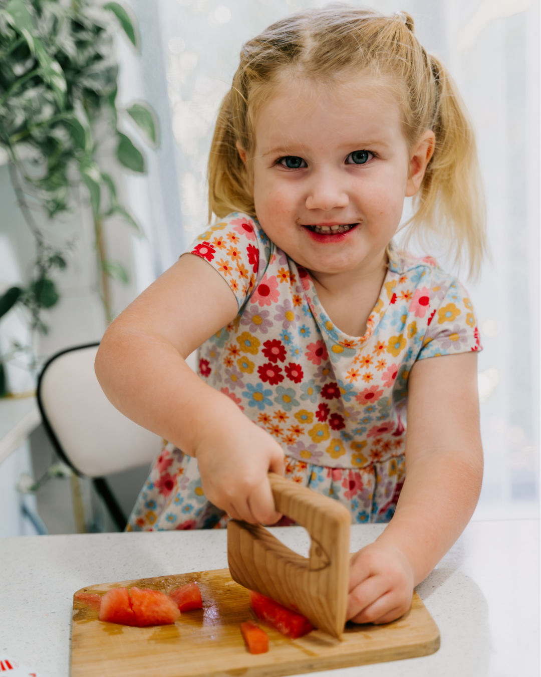 Young girl cutting watermelon with a wooden child-safe knife