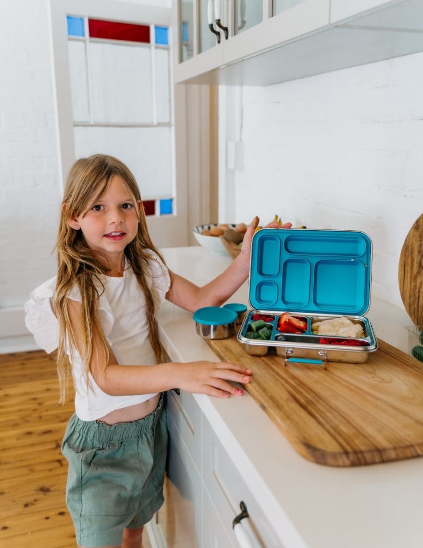 Introducing the Lunch Buddy Bento Set by The Play Way, a sleek rectangular stainless steel lunchbox with multiple compartments. The top right section is larger than the others, with "TPW" engraved in the central compartment. It features a silicone seal lid, rounded edge design, clasp closure, and a polished metallic finish.