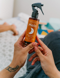 A 125 mL bottle of Melo Magnesium Sleep Spray with a black spray top. The label is orange with text that reads 