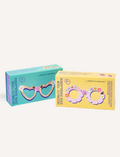 Two boxed craft kits feature a teal pair with heart-shaped sunglasses and a yellow pair with flower-shaped sunglasses. Both are labeled 