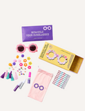 Two boxed craft kits feature a teal pair with heart-shaped sunglasses and a yellow pair with flower-shaped sunglasses. Both are labeled 