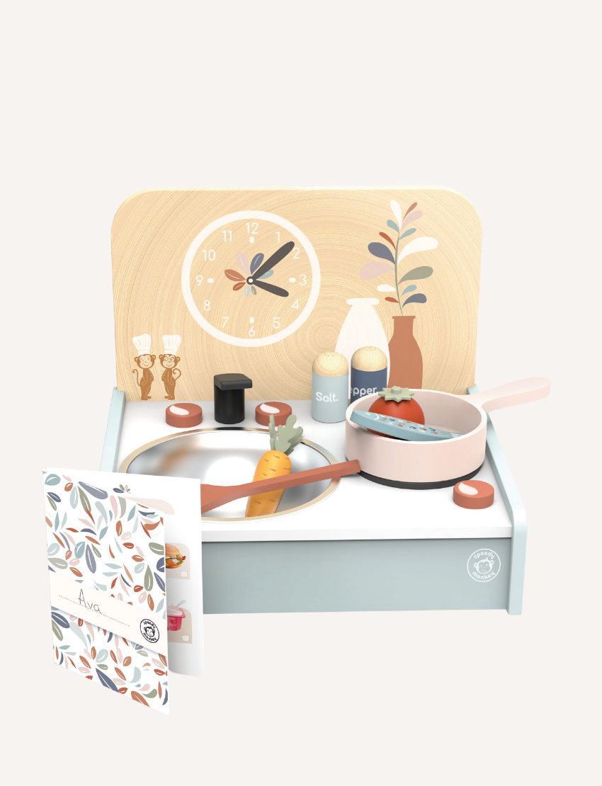 The Speedy Monkey Table Kitchen with 8 accessories is a children's wooden portable kitchen set that includes a stove complete with utensils, a pan, and pretend food. Made from FSC® certified wood, the design incorporates a backdrop featuring a clock and decorative elements. A booklet adorned with floral designs adds to this charming play area.