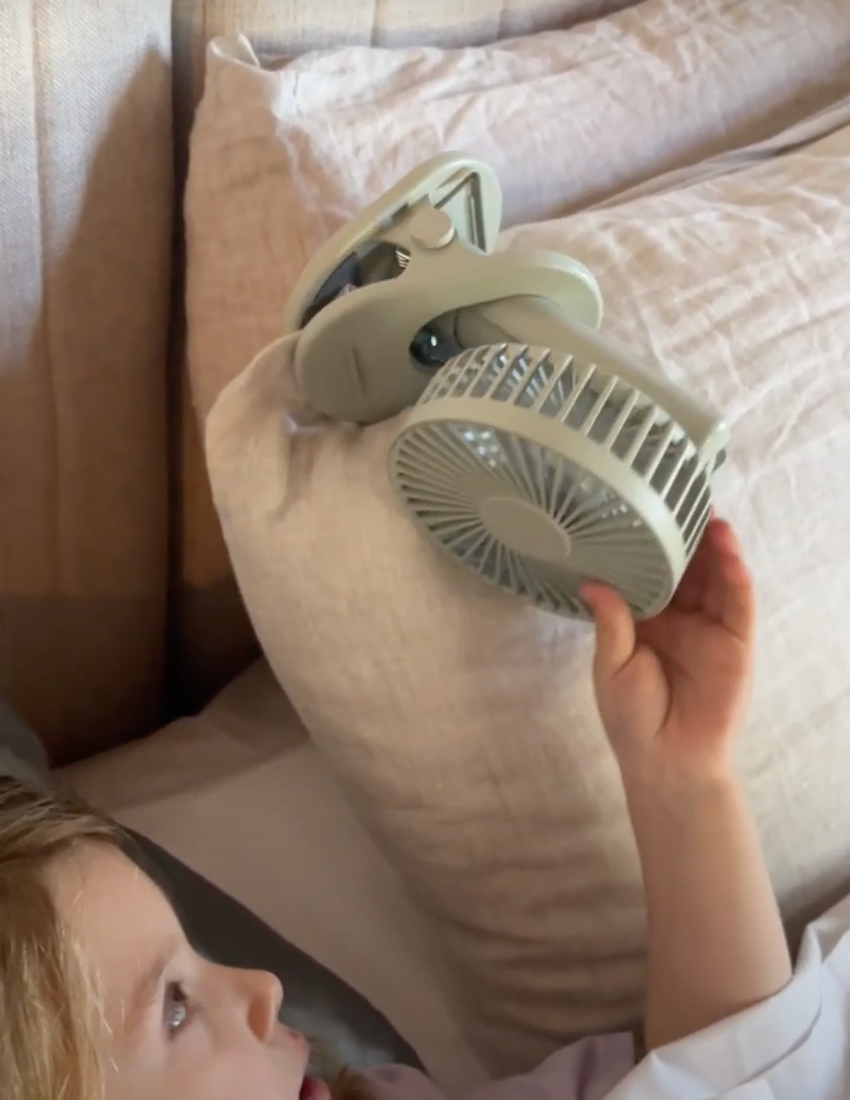 A small, gray, Sensory Play Australia Sleep Fan with a circular blade guard and a clip base stands upright on a white background. This portable fan produces gentle white noise and features a power button on the front, making it perfect for creating a calming atmosphere.