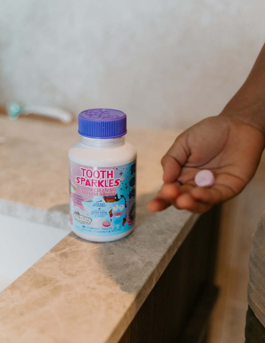 A white bottle with a purple cap is labeled "Tooth Sparkles - Tooth Cleaning Chews" by Jack N' Jill. The label showcases colorful illustrations of planets and characters. It contains 60 chewable tablets enriched with calcium, vitamin D, and xylitol, offering sensory-friendly dental care for strong teeth.