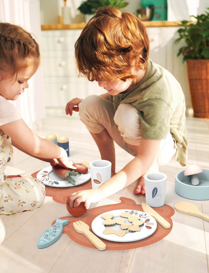 The Speedy Monkey Dining Set, crafted from sustainably sourced wood, includes two placemats shaped like animal heads and comes with plates, cutlery, and toy food items such as a carrot, fish, and cookie. This delightful role play experience is rounded out with a toy pan, salt and pepper shakers, cups, and additional utensils.