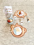 The Speedy Monkey Dining Set, crafted from sustainably sourced wood, includes two placemats shaped like animal heads and comes with plates, cutlery, and toy food items such as a carrot, fish, and cookie. This delightful role play experience is rounded out with a toy pan, salt and pepper shakers, cups, and additional utensils.