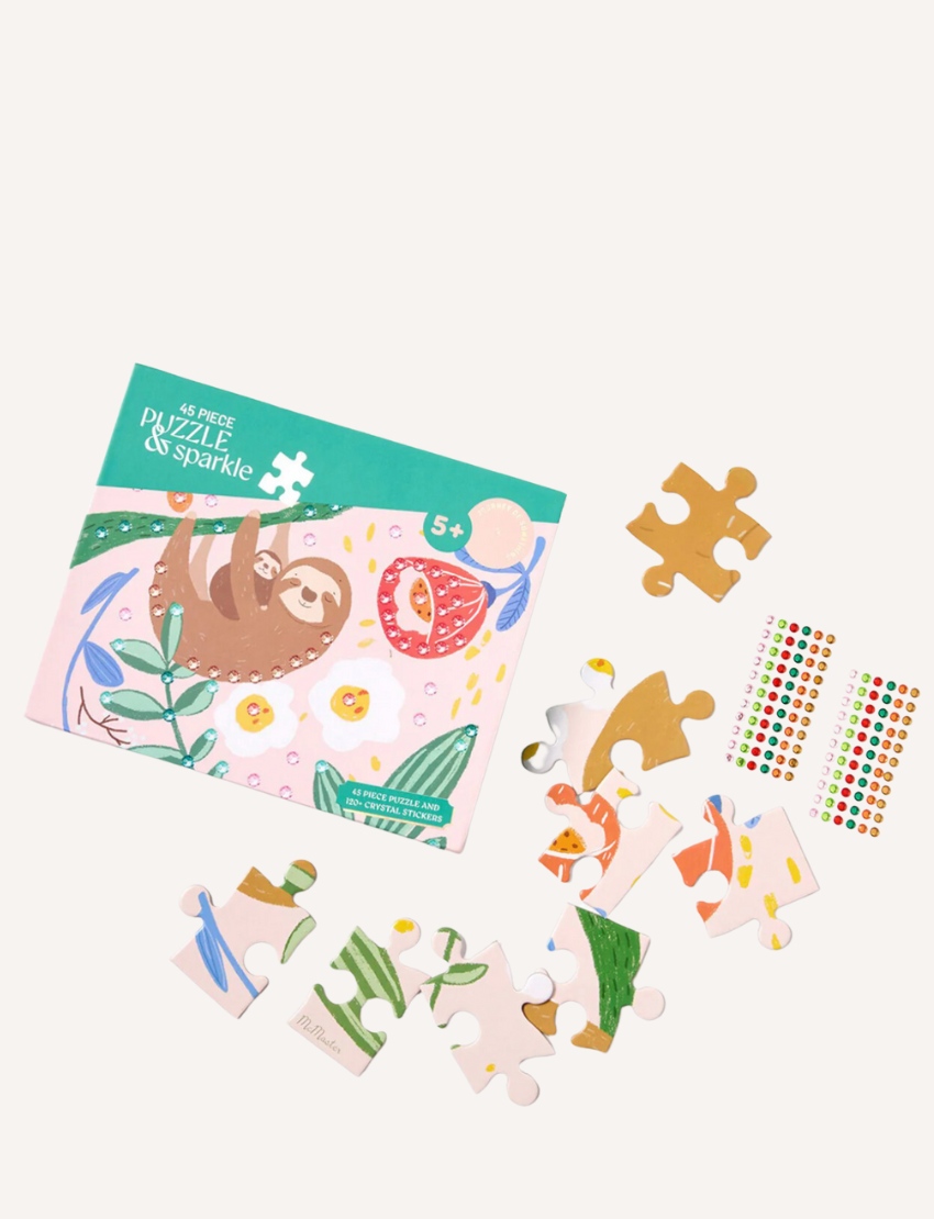 A 45 Piece Kids Puzzle with Gems by Journey of Something comes in a colorful box adorned with a sloth illustration. Alongside the box, you'll find several puzzle pieces arranged nearby and a sheet of vibrant, small stickers. This sloth-themed puzzle is designed for ages 5 and up.