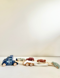 The Speedy Monkey Car Transporter is a wooden vehicle set that includes a blue toy truck with a double-deck trailer. It carries four vibrant wooden cars painted in red, green, orange, and maroon using non-toxic paint. The detachable trailer also features a white support frame for enhanced stability.