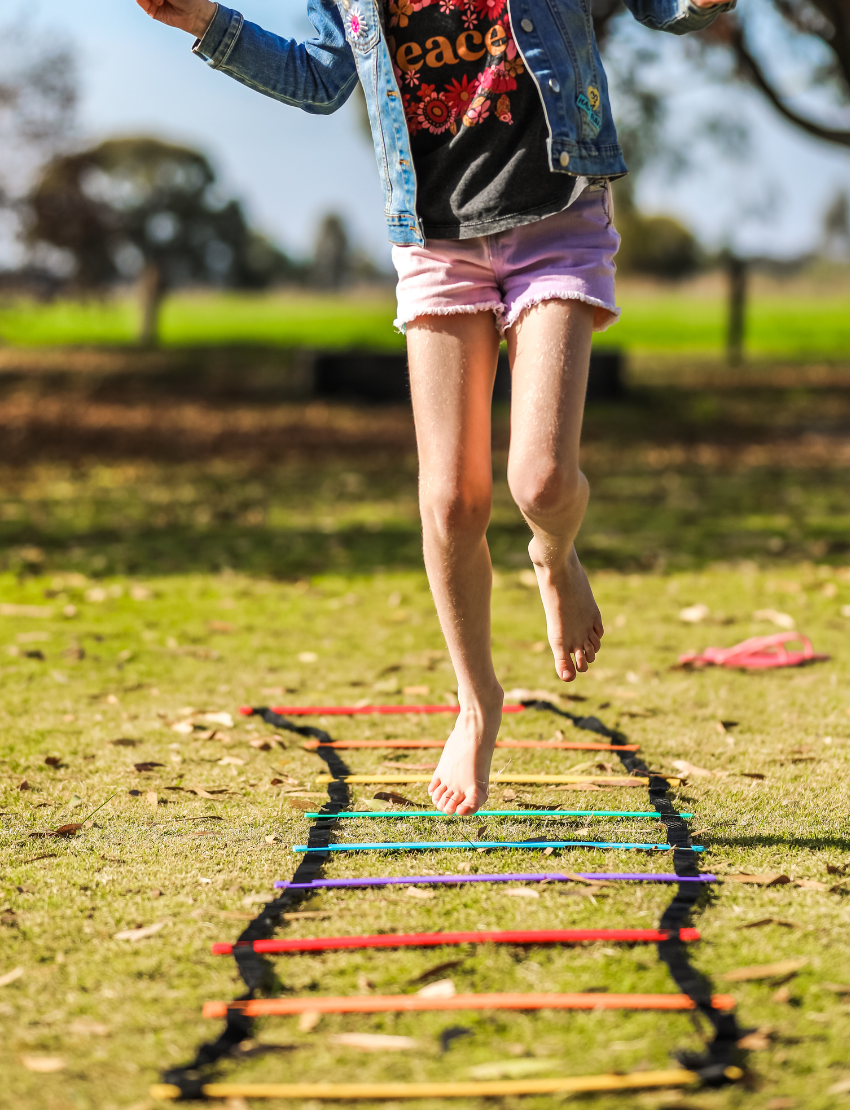 Seven Rainbow Ladders from Hart Sport are arranged in a fan shape, each featuring a different vibrant color: red, orange, yellow, green, blue, purple, and pink. These ladders include black straps at the ends.