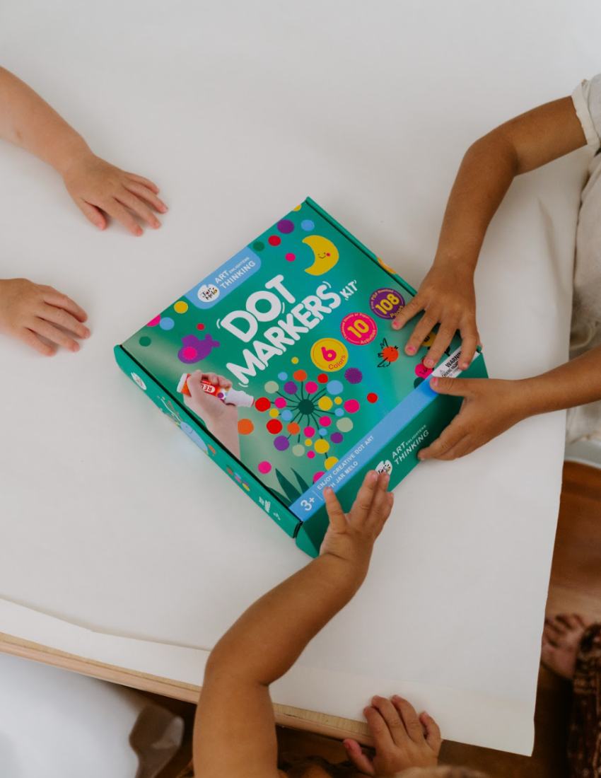 A large green box contains children's art supplies designed to foster creative expression: it features the Jar Melo Fine Motor Practice: Puzzle and Art Kit, which includes a pack of Giant Finger Paint Paper with a blue octopus and yellow crocodile, a Dot Painting Kit filled with colorful dots, and animal-themed tools that enhance fine motor skills.