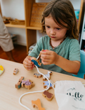 The Play Way's Fine-Motor Practice: Puzzle and Craft Kit is a large open green box designed to enhance sensory-rich creativity and early learning. It includes a variety of children's art supplies such as a coloring book, a finger paint set, colored shapes, markers, and activity cards, all showcased against a plain white background.