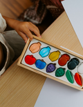 The Play Way's Fine-Motor Practice: Puzzle and Craft Kit is a large open green box designed to enhance sensory-rich creativity and early learning. It includes a variety of children's art supplies such as a coloring book, a finger paint set, colored shapes, markers, and activity cards, all showcased against a plain white background.