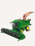 A Bruder John Deere Combine Harvester in green, complete with yellow wheels, is showcased with its header detached and positioned beside it. This T 670i model features a meticulously detailed exterior that captures the essence of traditional agricultural machinery.