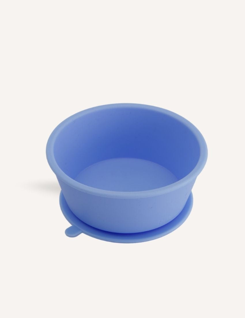 An open green and teal cardboard box from The Play Way's Tools For Eating - Bowls & Plates Kit contains a set of stackable silicone suction bowls, a set of stackable cups, and an upright blue divided baby plate. The items are neatly arranged, showcasing their self-feeding design.