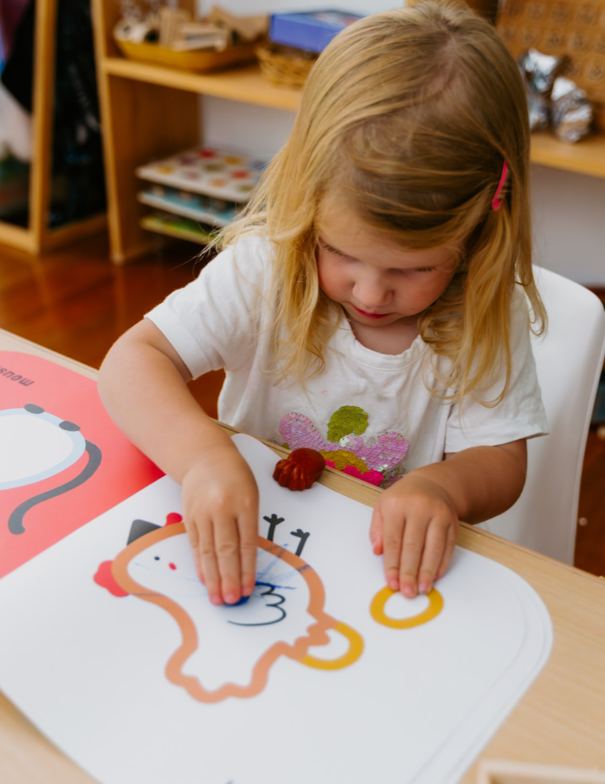 The Play Way's Fine-Motor Practice: Puzzle and Craft Kit is a large open green box designed to enhance sensory-rich creativity and early learning. It includes a variety of children's art supplies such as a coloring book, a finger paint set, colored shapes, markers, and activity cards, all showcased against a plain white background.