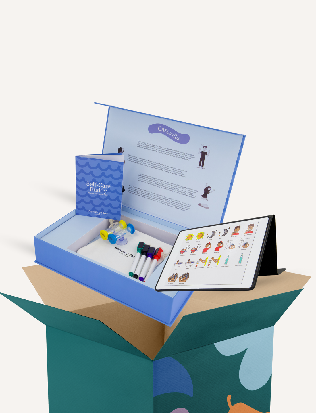 An open box featuring The Play Way’s "Self-Care Buddy" kit, which includes a booklet titled "Self-Care Buddy," markers, and a tablet displaying a chart with various symbols. The lid of the box is adorned with text and illustrations, and the entire setup is placed within a larger, partially visible green and blue box.