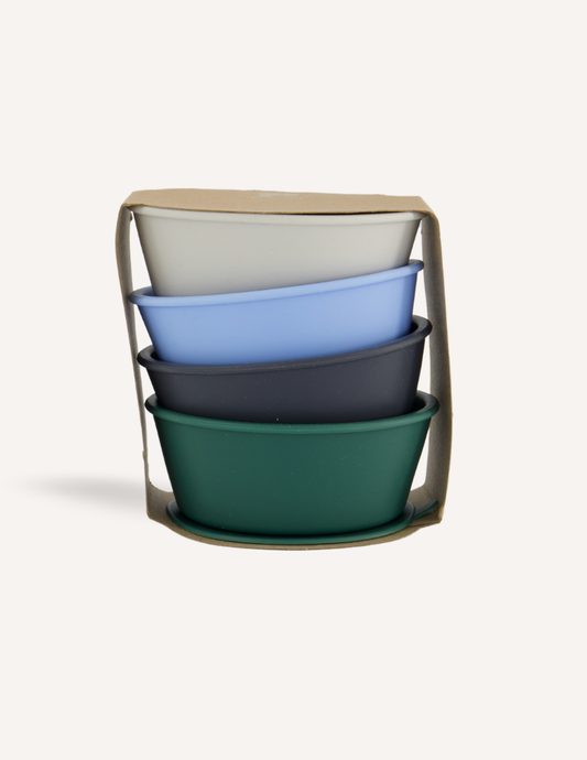 A set of four Silicone Suction Bowls by Preppit, featuring an array of colors (white, light blue, dark blue, and green), neatly nested inside one another and packaged in a durable cardboard holder. The oval-shaped bowls are displayed against a plain white background.