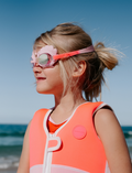 On a plain background, two pairs of Sunnylife's Mini Swim Goggles are displayed. The top pair is pink adorned with a shell design, while the bottom pair is blue with intricate shark details, including fins and teeth.