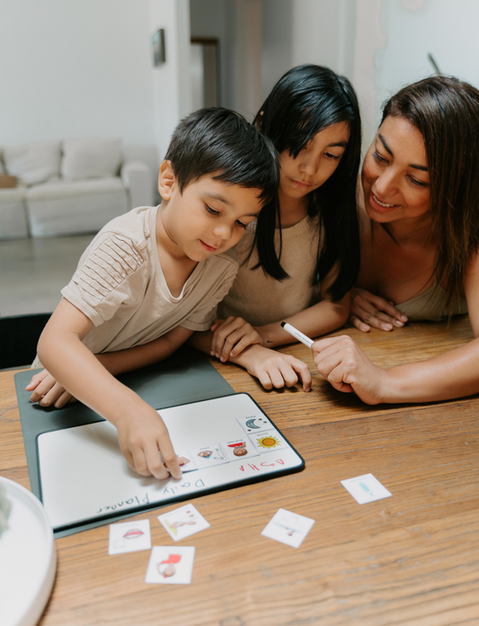 The "Self-Care Buddy Magnetic Planner Set" from Sensory Play Australia features a book and markers designed to encourage children's independence. They are displayed alongside an open tablet showcasing various icons, all elegantly placed on a larger decorative green box, enhancing the charm of this self-care setup.