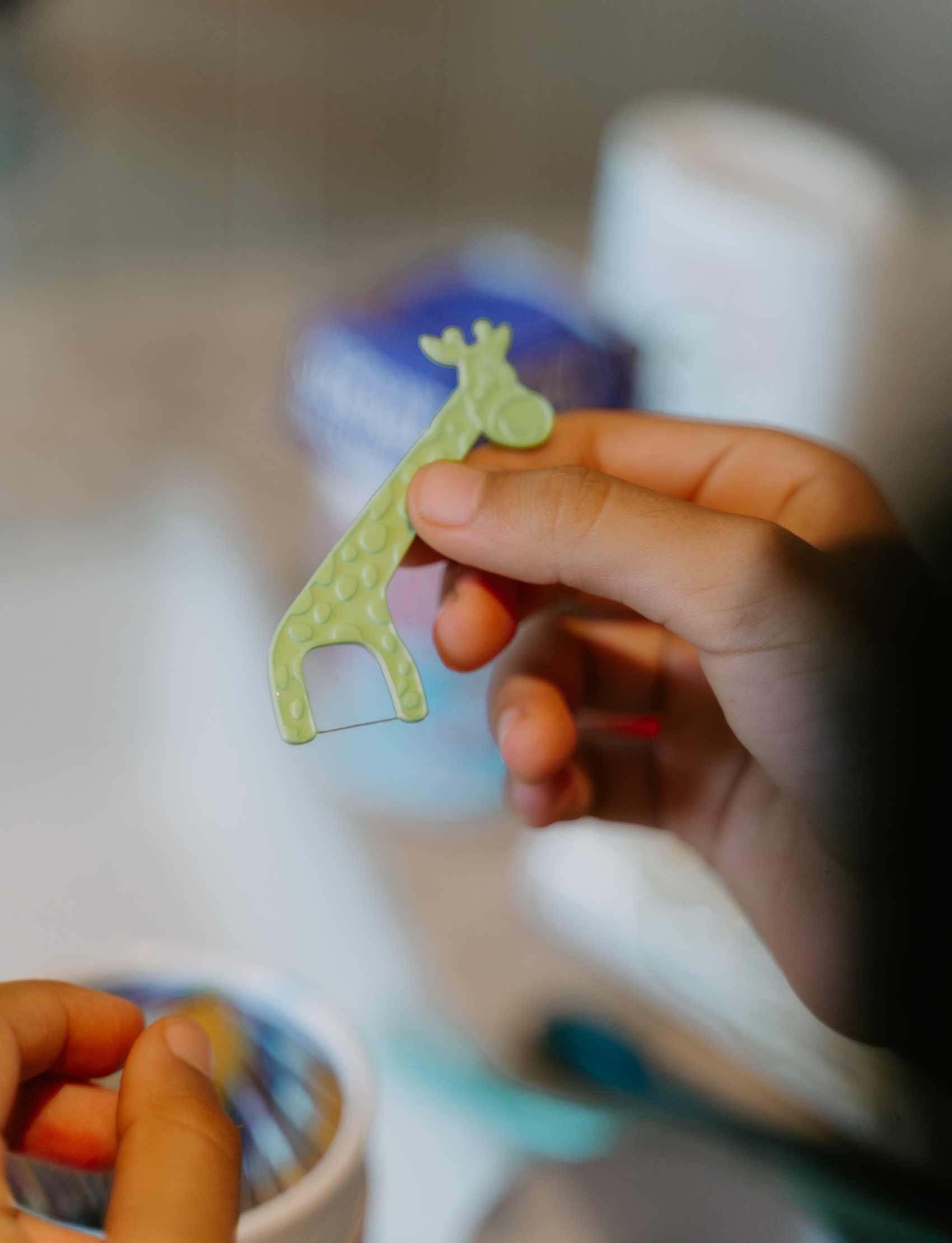 An open box containing various children's dental care products, including biodegradable toothbrushes, natural toothpaste, and floss. The Dental Care Kit by The Play Way includes items for different age groups, ranging from 6-12 months to 2-5 years, along with silicone finger brushes and biodegradable floss picks.