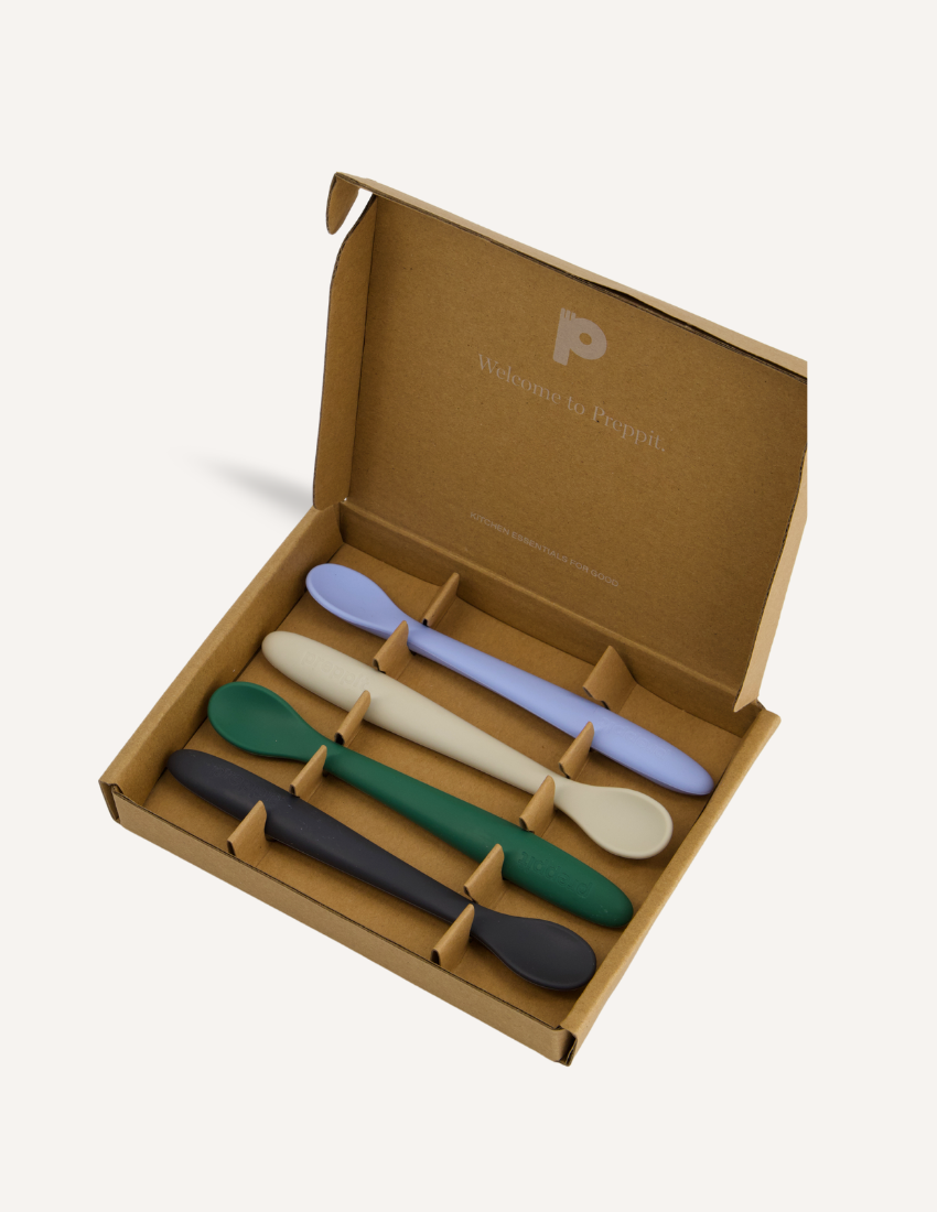 The Sensory Friendly Food Handling Kit by The Play Way comes in a cardboard box containing an assortment of kitchen utensils, ideal for enhancing fine motor skills. It includes peelers, fruit sticks, and a versatile kitchen tool, all neatly displayed in open brown boxes with a green and blue patterned box beneath.