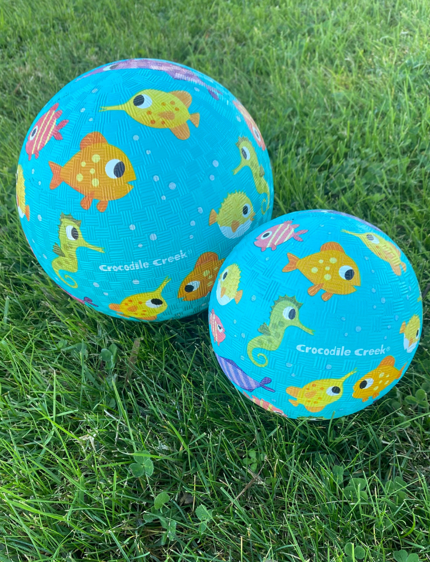 The Crocodile Creek 5 Inch Playground Ball is a yellow rubber ball with a textured surface adorned with vibrant illustrations of construction vehicles, including diggers and trucks, set against a simple light-colored background.