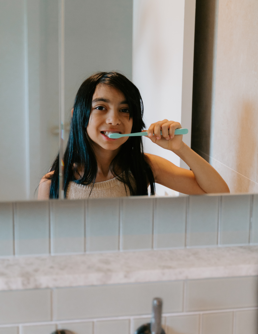 Young girl brushing her teeth in front of a bathroom mirror.