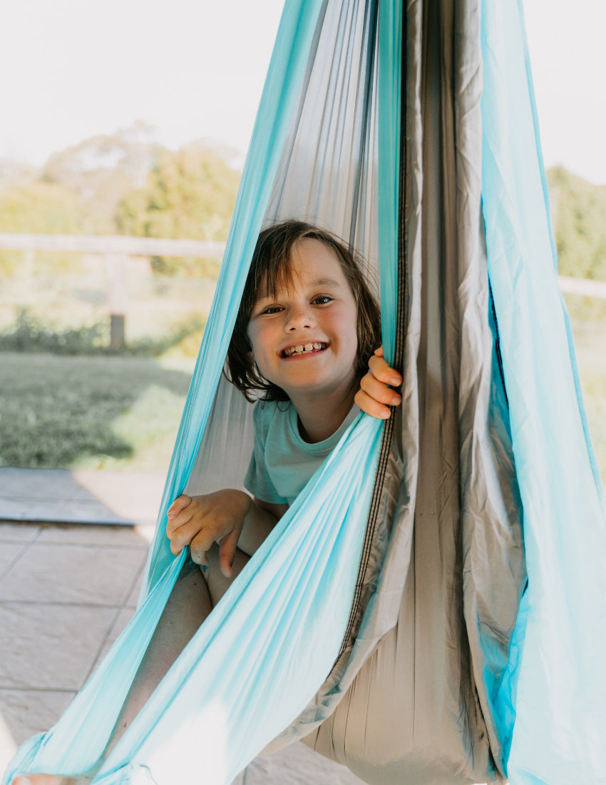 Smiling child peeking out from a colorful fabric swing or hammock.