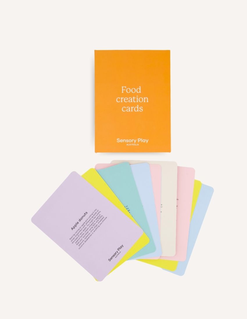 The image displays two orange items titled "Food Creation Cards Set in Box" by Sensory Play Australia. The smaller box is positioned on the left with its lid closed, while the larger box stands upright on the right. Both items, ideal for culinary creativity, are set against a plain white background.